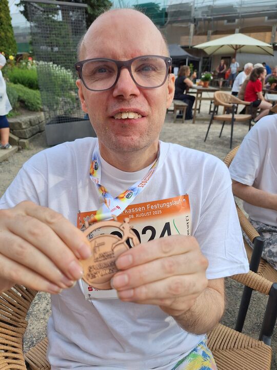 Das Bild zeigt einen Mann, der eine Medaille in die Kamera zeigt.